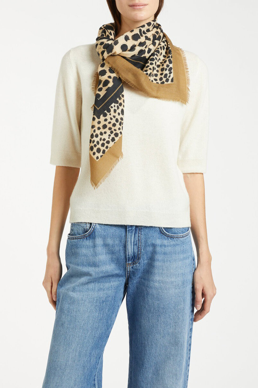 Person wearing a beige sweater, blue jeans, and a patterned scarf on a white background