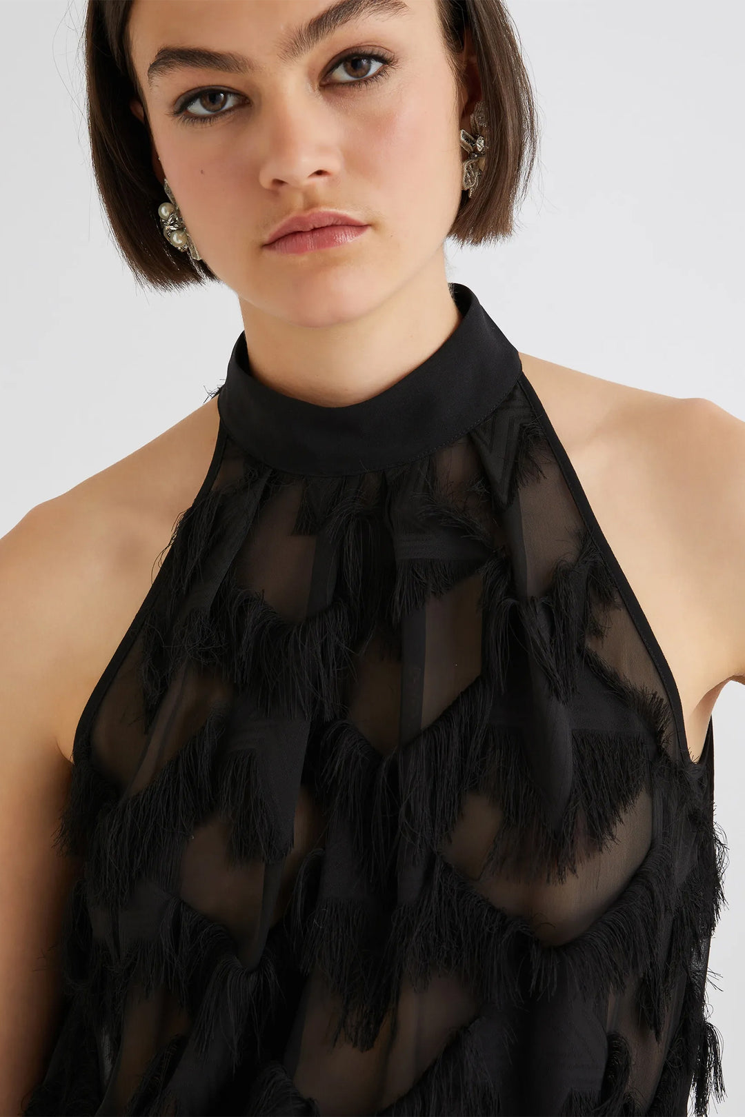 Woman wearing a black halter top with fringe details on a white background