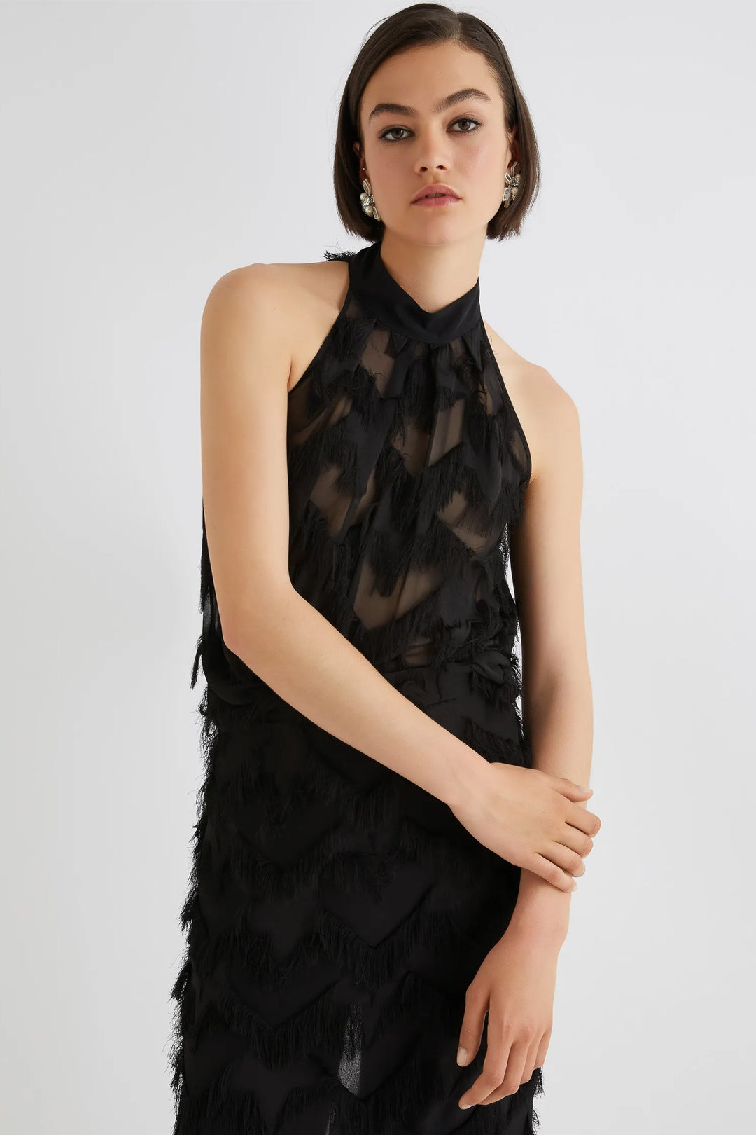 Woman wearing a black halter neck dress with feather details on a white background