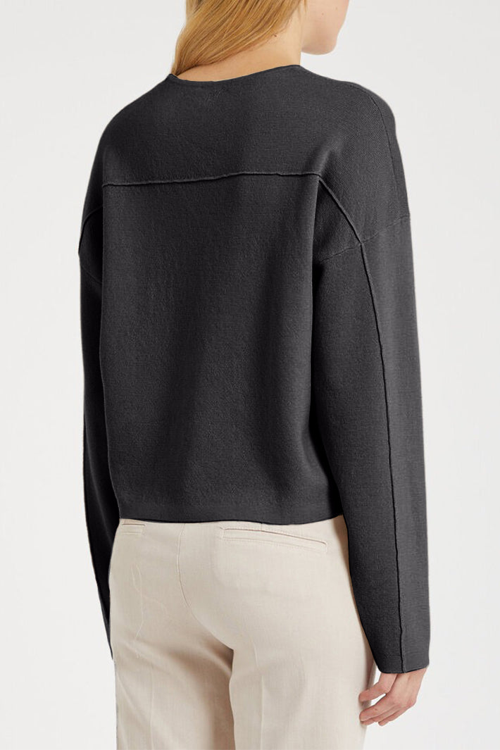 Person wearing a black long-sleeve top and beige pants on a white background