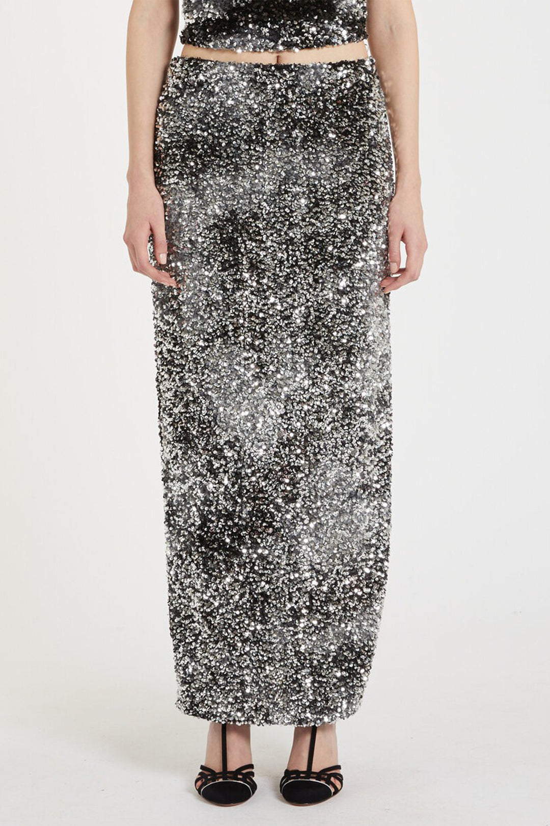 Person wearing a long, sparkling black and silver sequin skirt on a white background