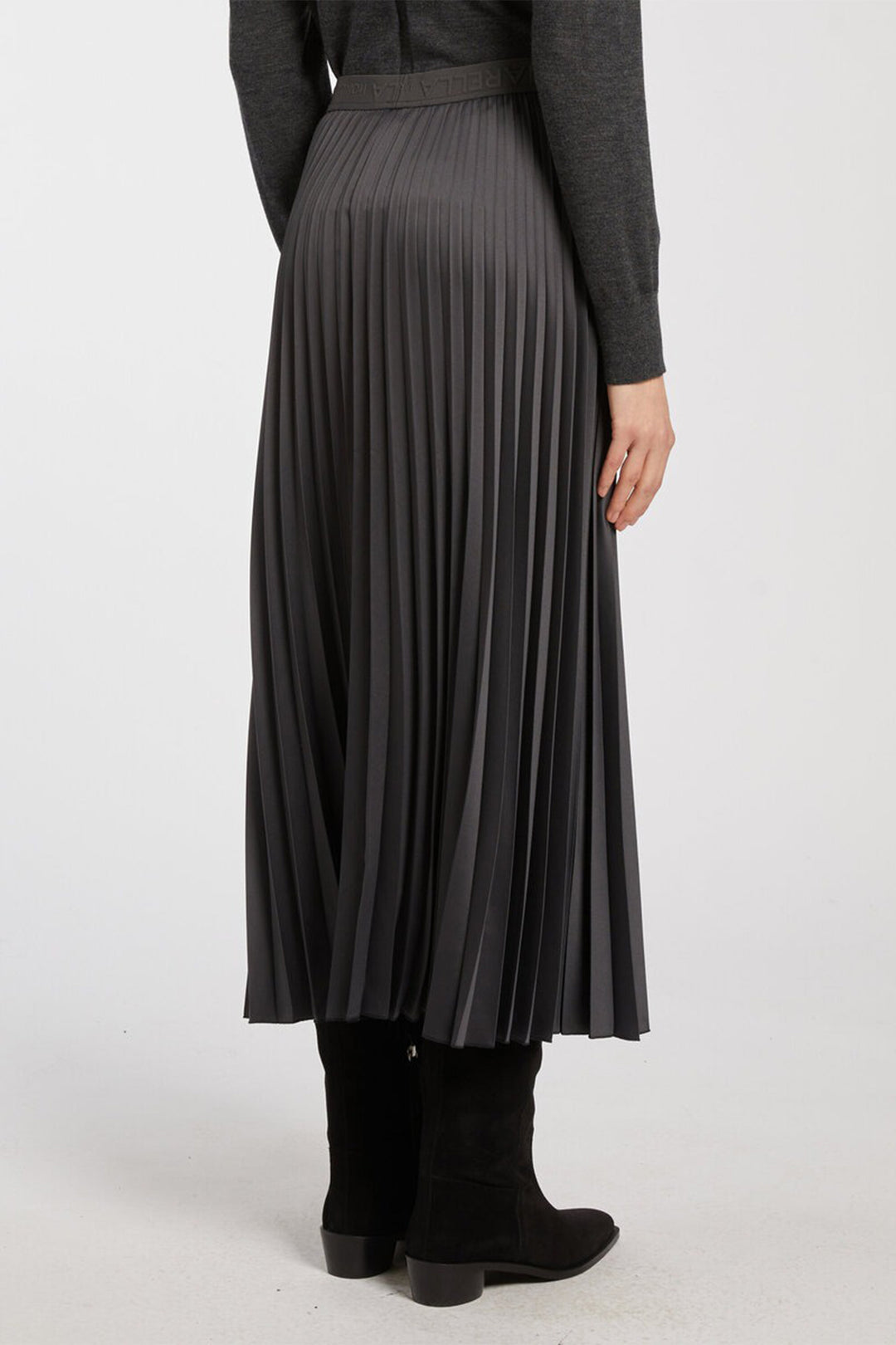 Person wearing a long pleated skirt with a plain background