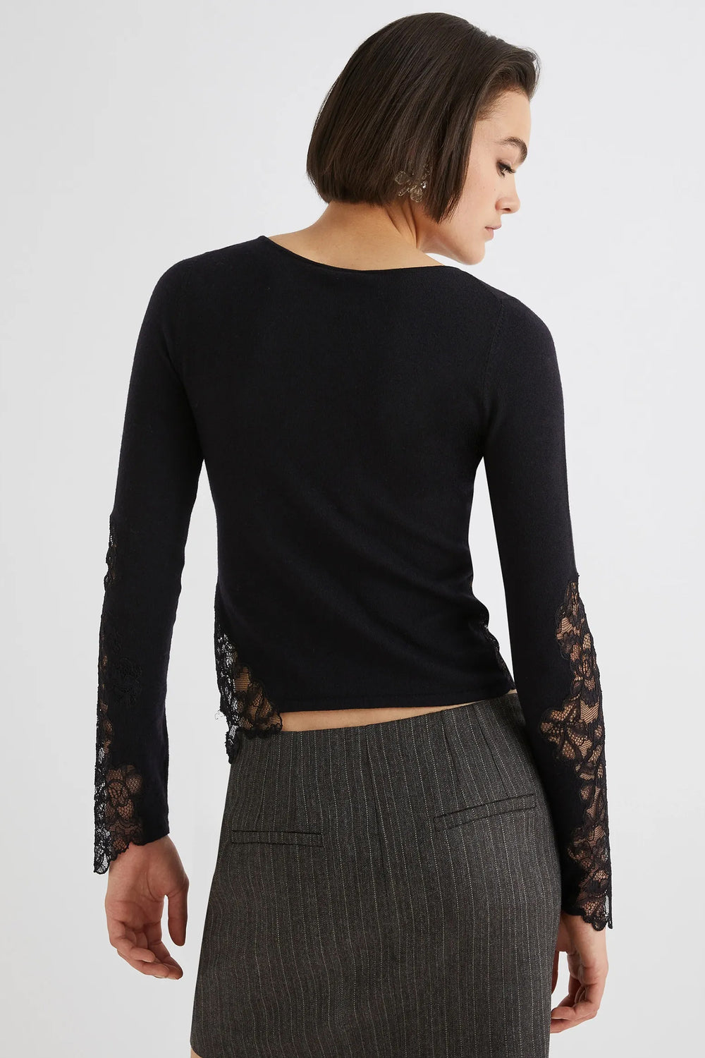 Woman wearing a black long-sleeve top with lace sleeves on a white background