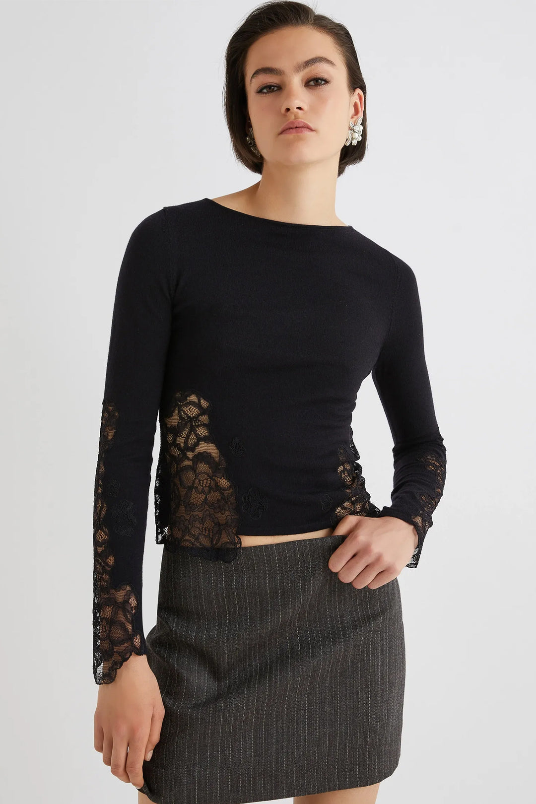 Woman wearing a black long-sleeve top with lace details and a gray skirt on a white background