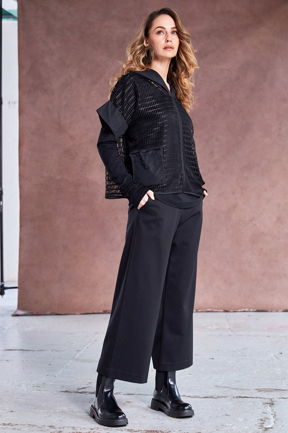 Woman wearing a black outfit standing against a brown wall.
