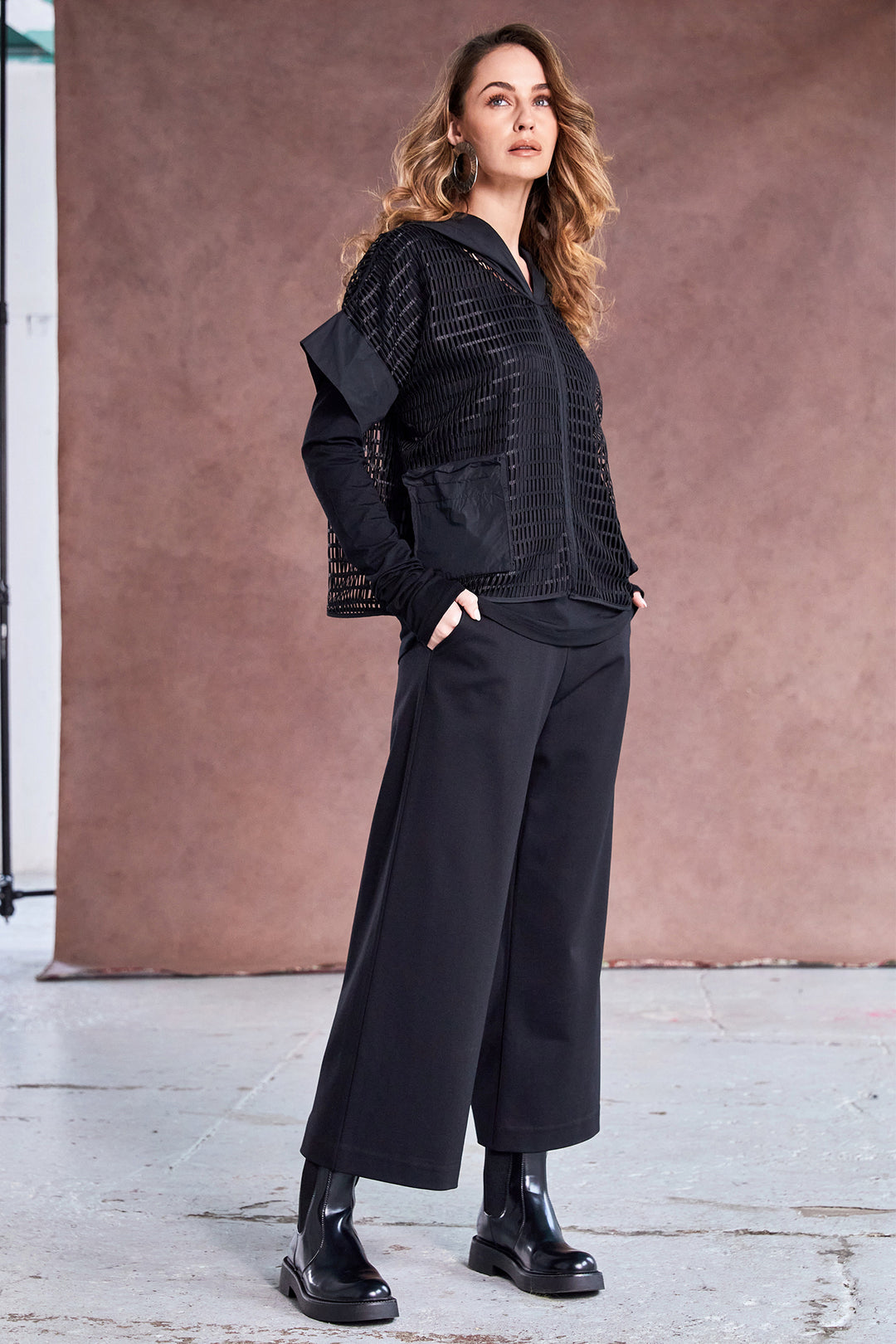 Woman wearing a black outfit standing against a brown wall.