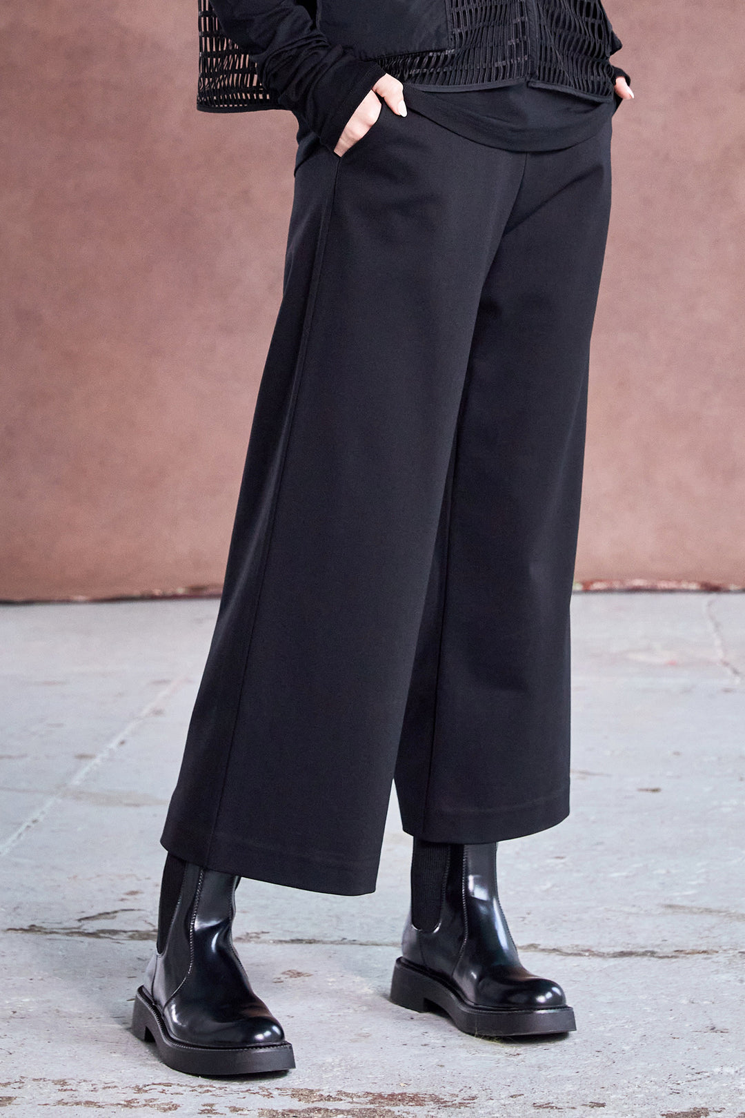 Person wearing black wide-leg pants and black shoes against a pink wall.