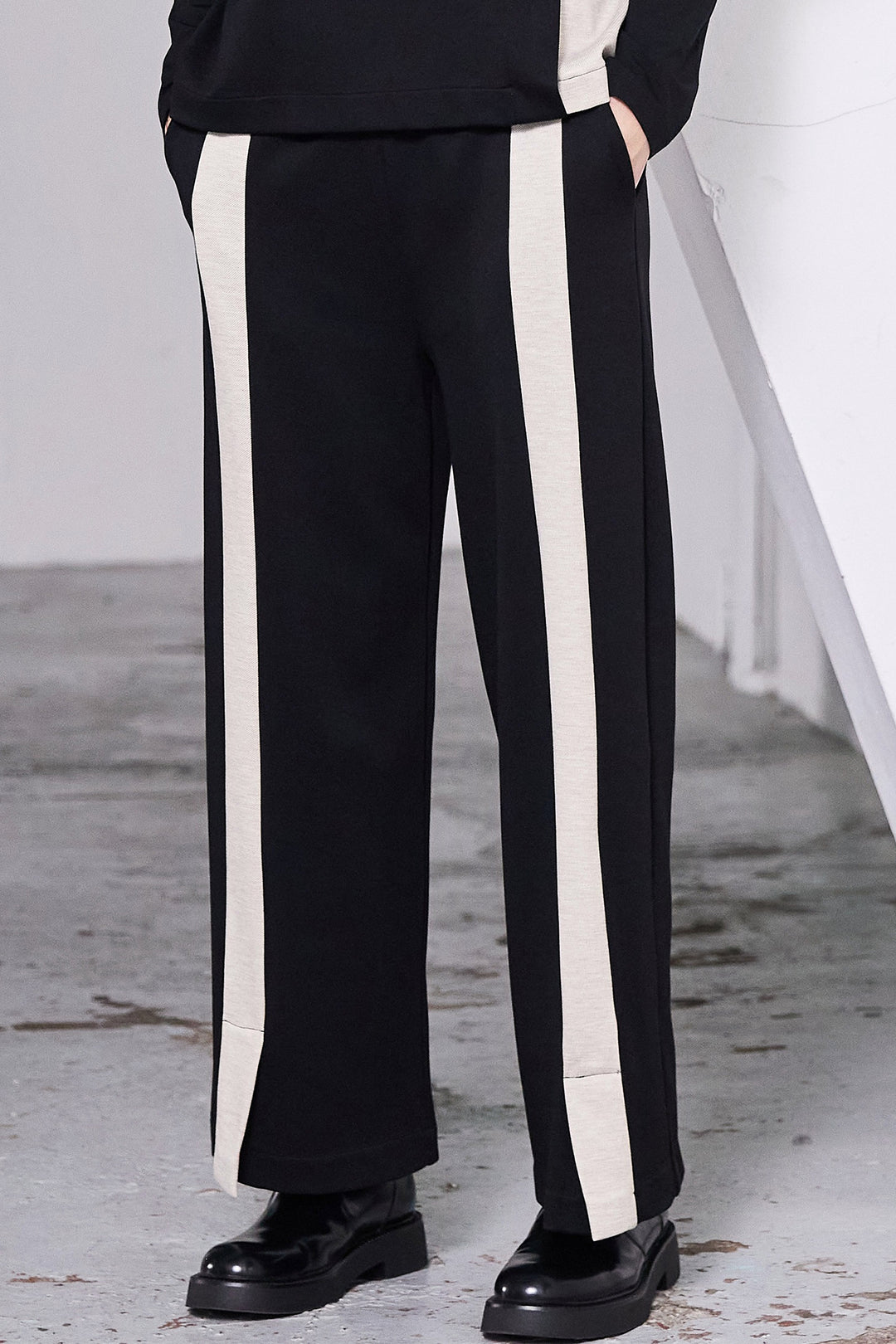 Black pants with white stripes worn by a person on a concrete floor.
