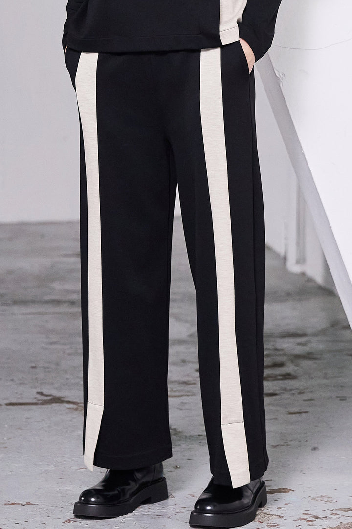 Black pants with white stripes worn by a person on a concrete floor.