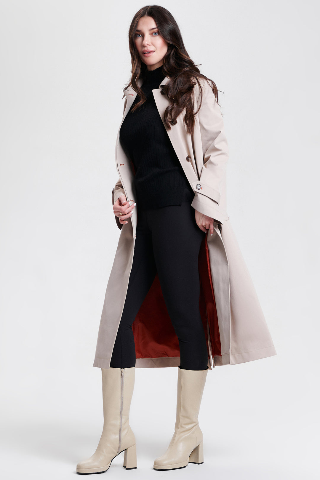 Woman wearing a beige trench coat, black top, red skirt, and white boots on a white background