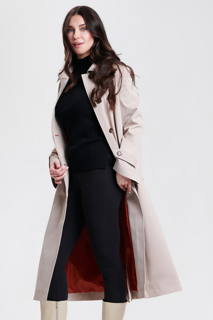 Woman wearing a beige trench coat over a black outfit with red lining on a white background