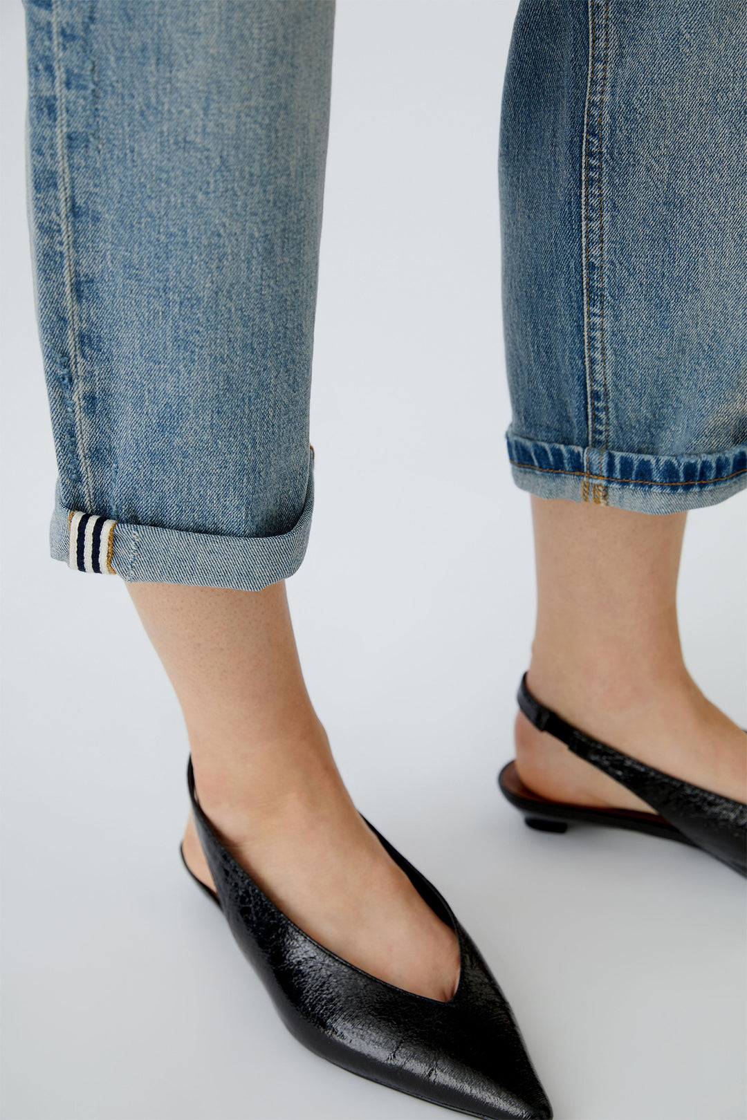 Black pointed-toe flats worn with rolled-up jeans on a white background
