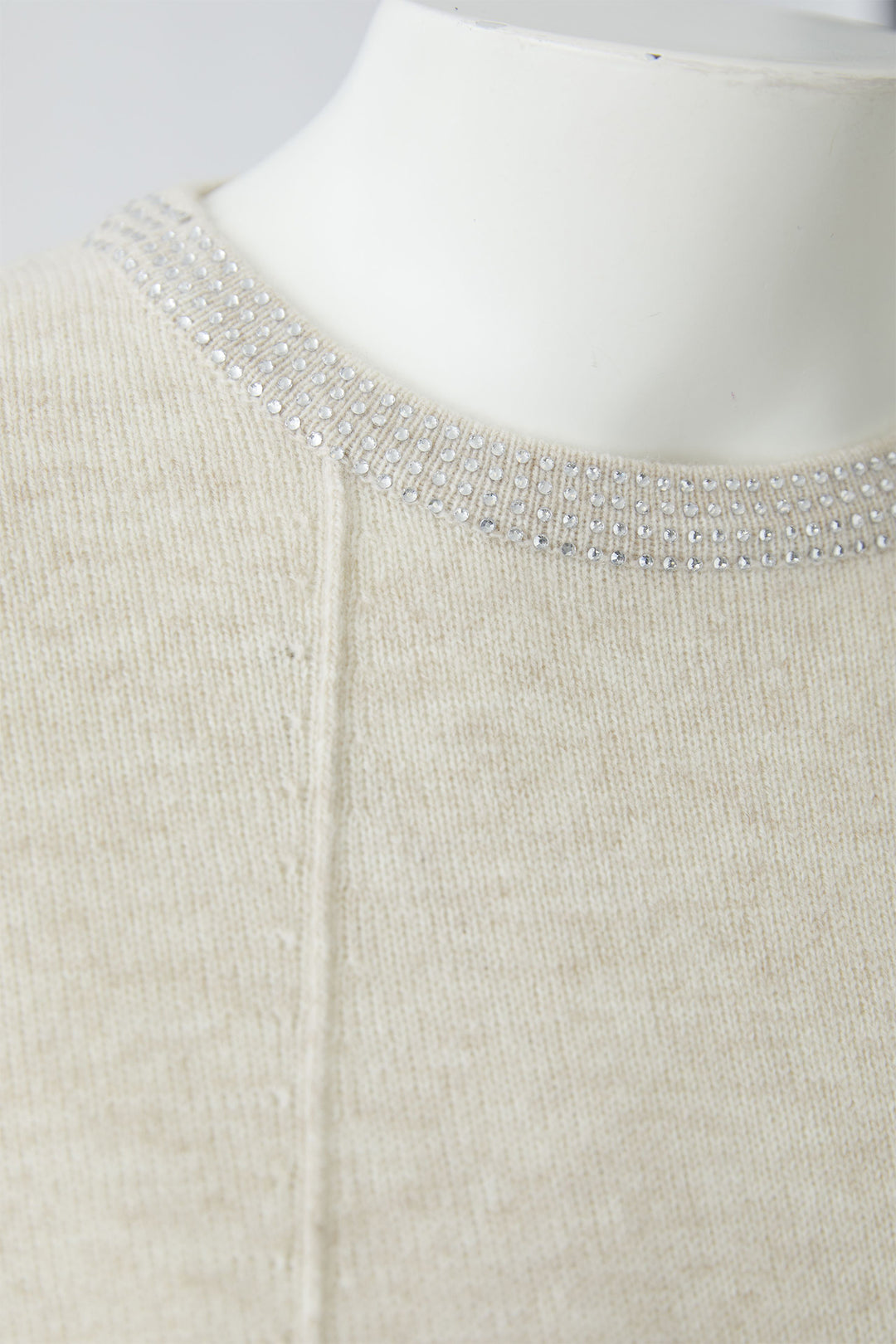 Close-up of a beige jumper with a beaded neckline on a mannequin.