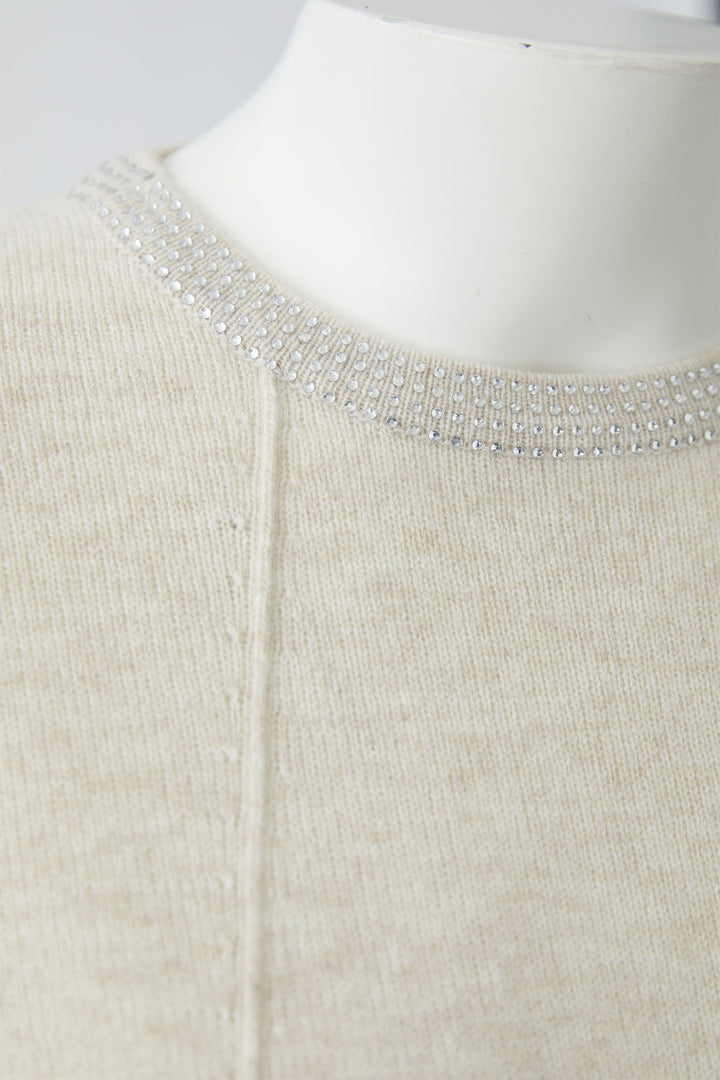 Close-up of a beige jumper with a beaded neckline on a mannequin.