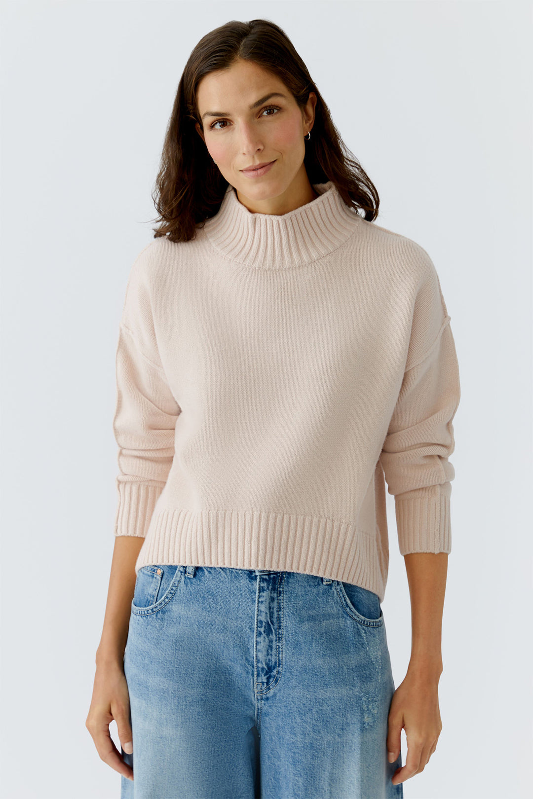 Woman wearing a beige sweater and blue jeans against a white background