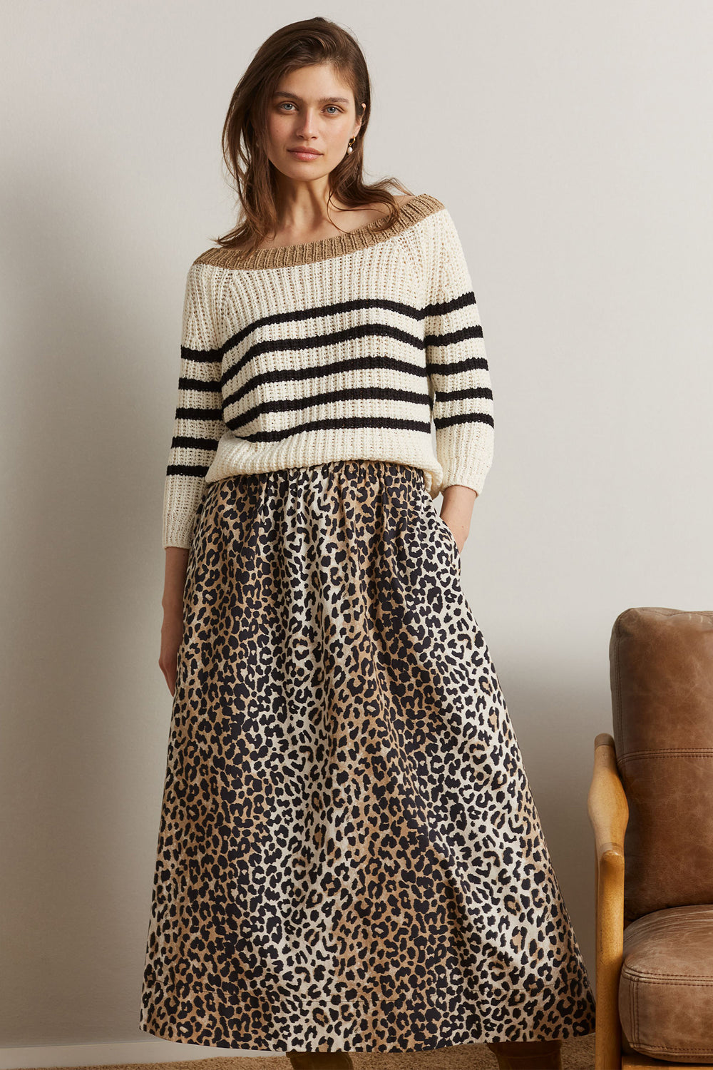 Woman wearing a striped sweater and leopard print skirt against a neutral background
