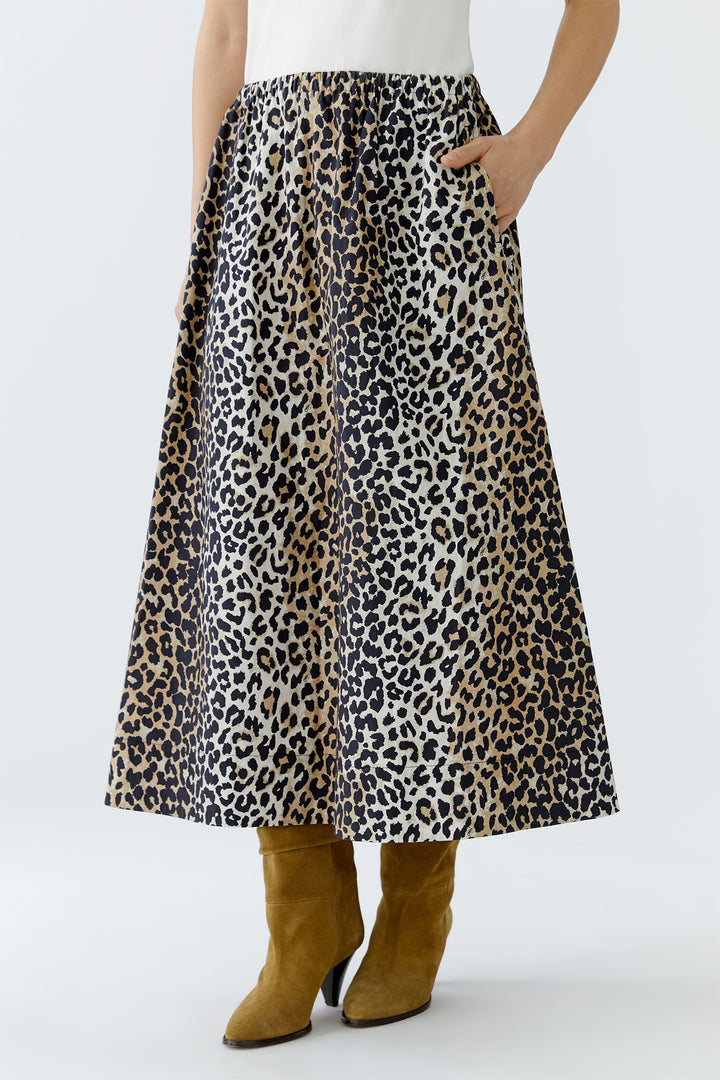 Person wearing a leopard print skirt with a white top and brown boots on a light gray background