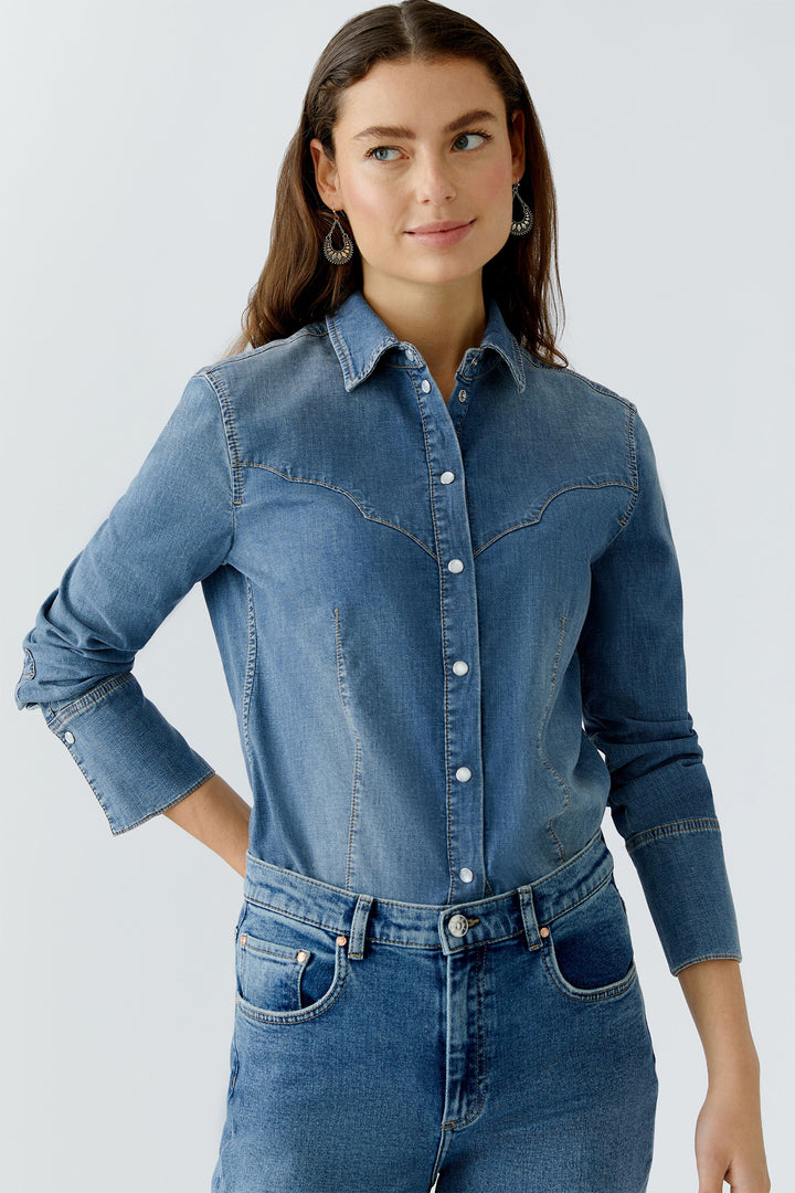Woman wearing a blue denim shirt and jeans on a light gray background