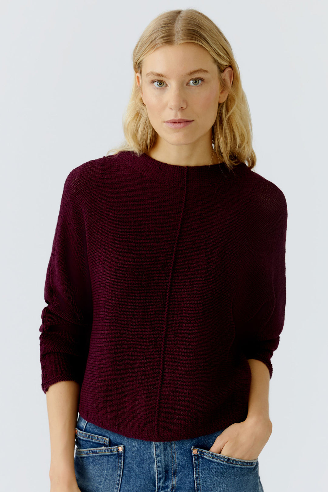 Woman wearing a burgundy sweater and blue jeans against a white background