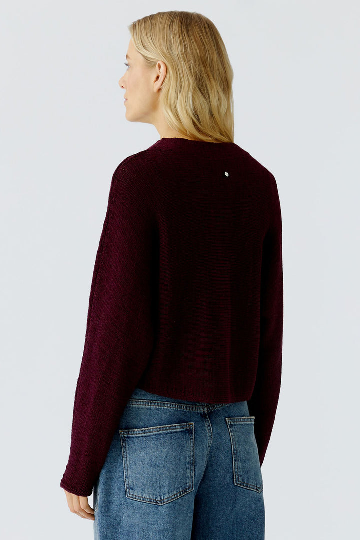 Woman wearing a dark red sweater and blue jeans on a light gray background