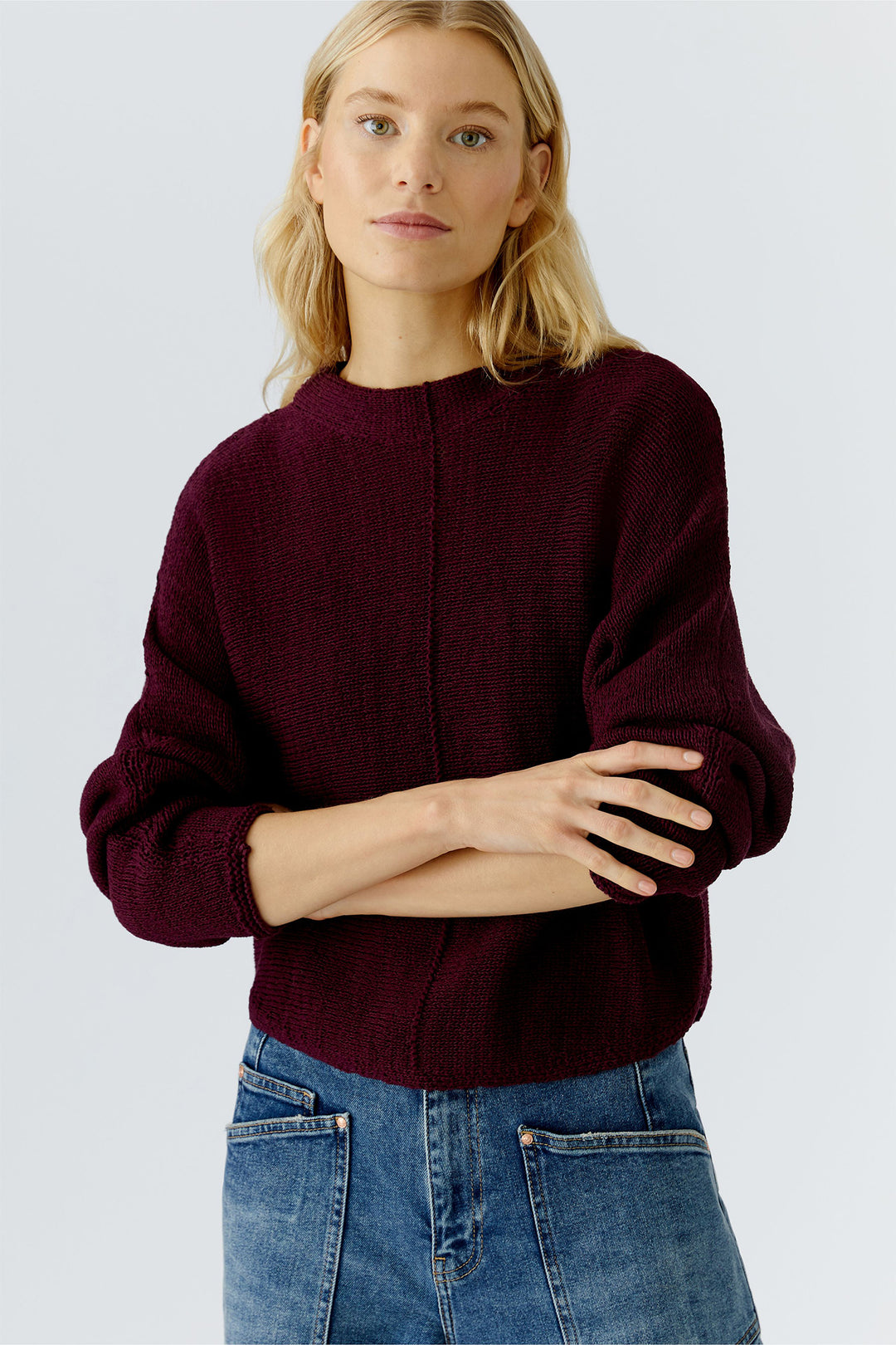 Woman wearing a burgundy sweater and blue jeans on a light gray background