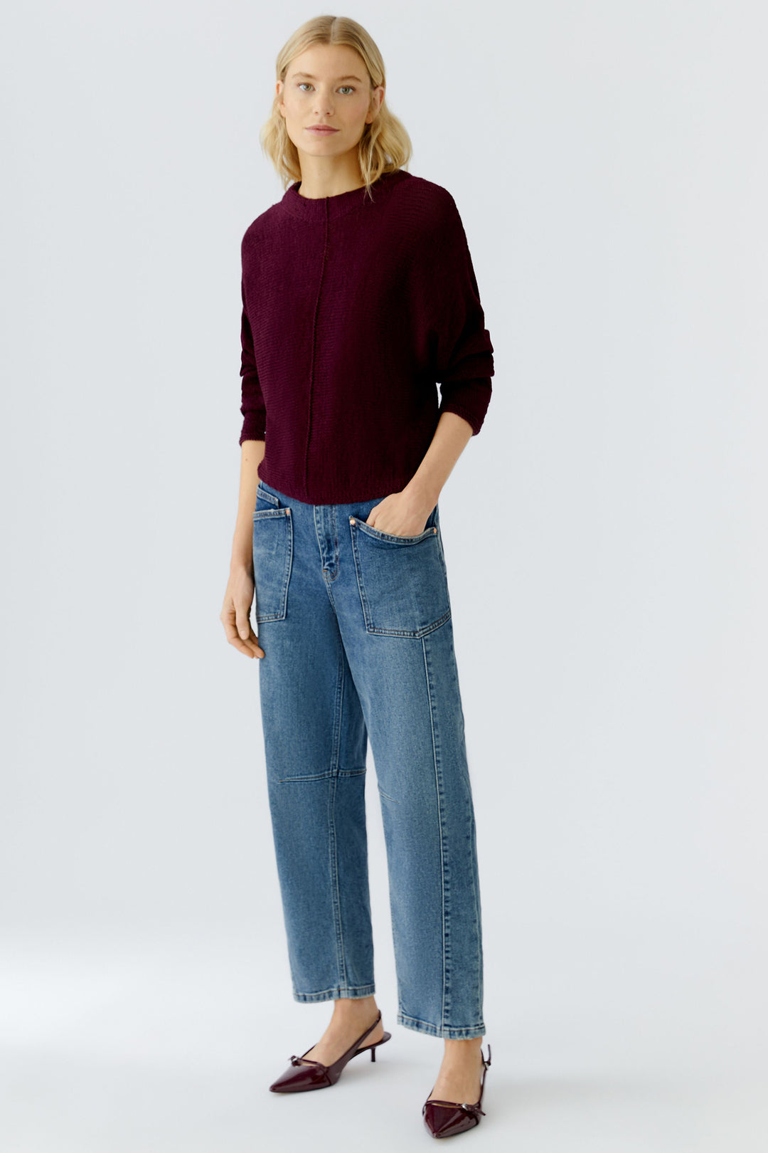 Woman wearing a burgundy sweater and blue jeans on a white background