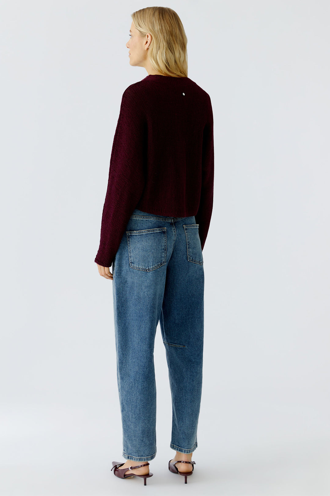 Person wearing a burgundy sweater and blue jeans on a white background