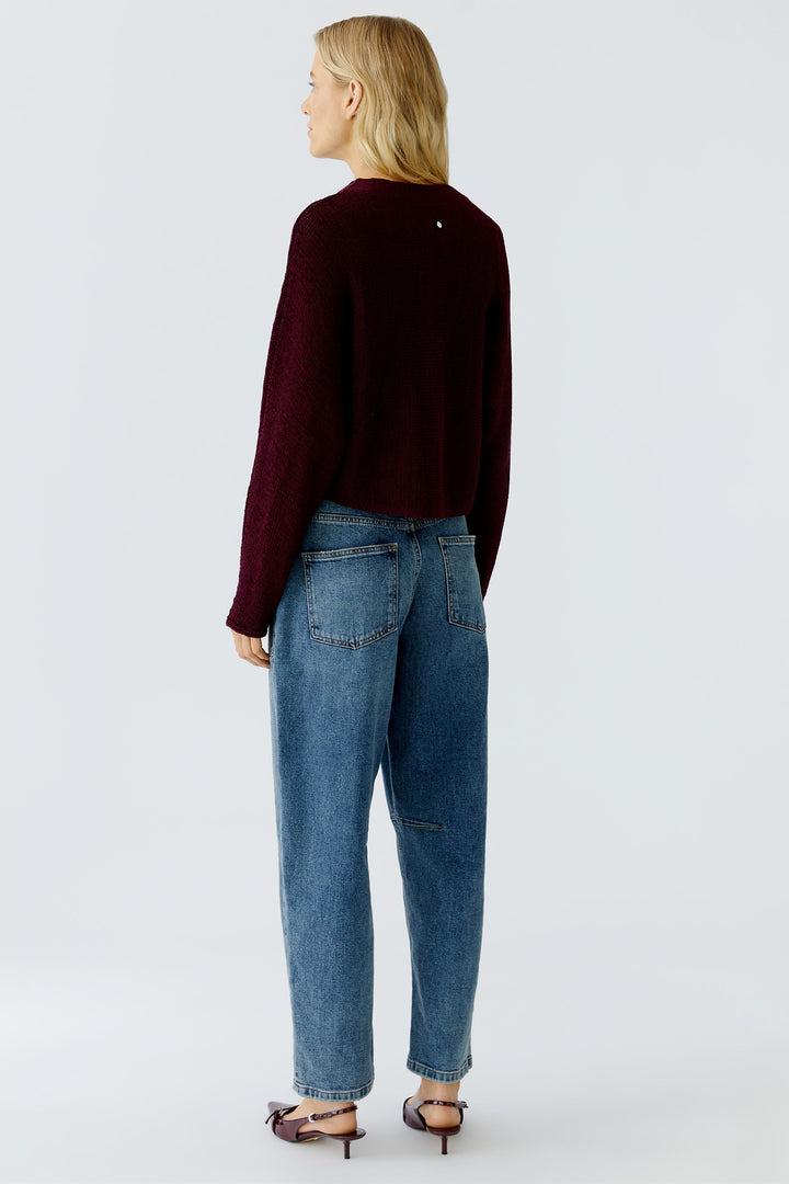 Person wearing a burgundy sweater and blue jeans on a white background
