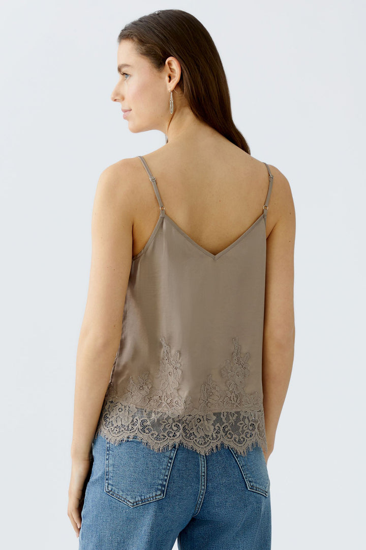 Woman wearing a beige lace-trimmed camisole and blue jeans on a light gray background