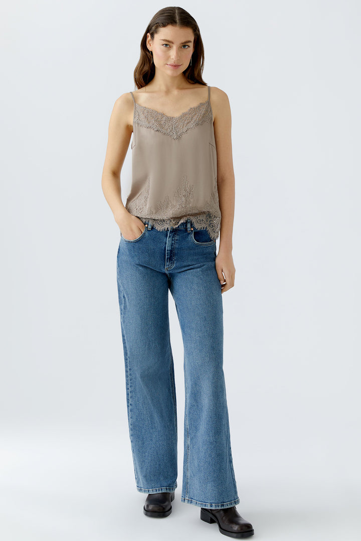 Woman wearing a beige lace top and blue jeans on a white background