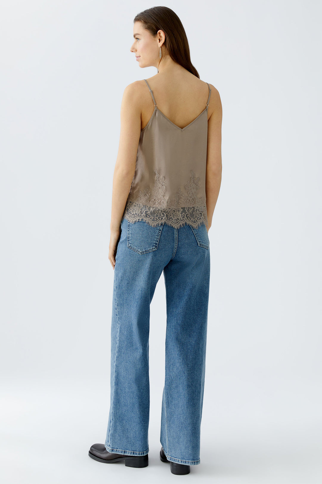 Woman wearing a beige lace top and blue jeans on a white background