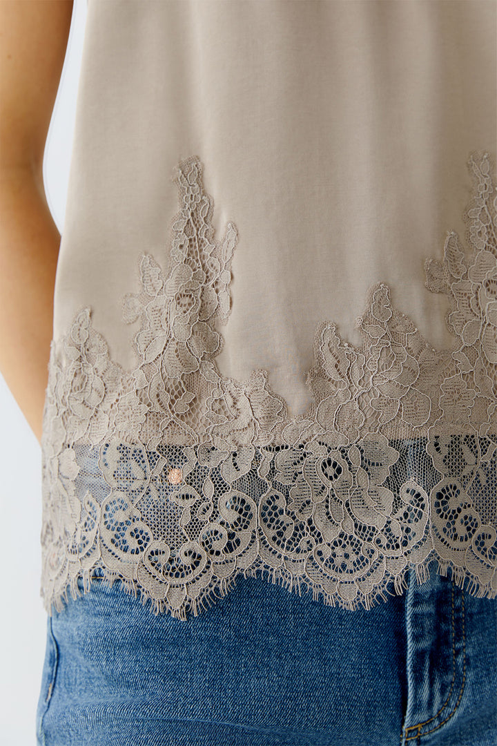 Close-up of a beige sleeveless top with lace detailing and blue jeans.