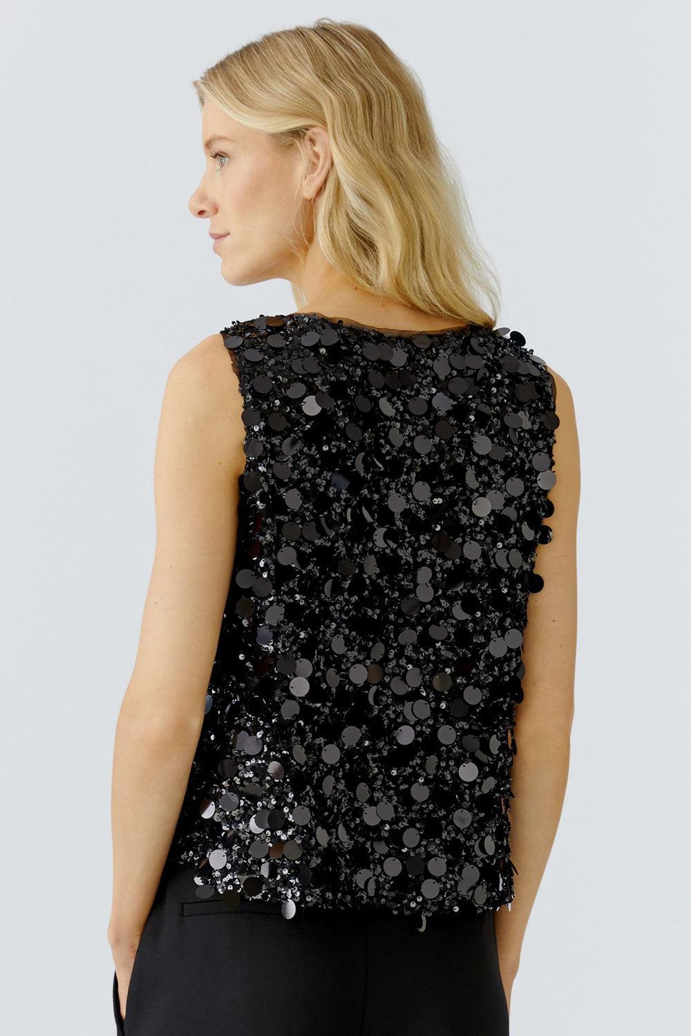 Black sequin sleeveless top worn by a person on a light gray background