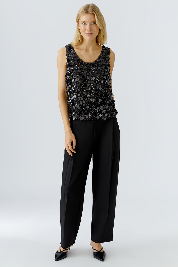 Woman wearing a black sequin top and black pants on a light gray background