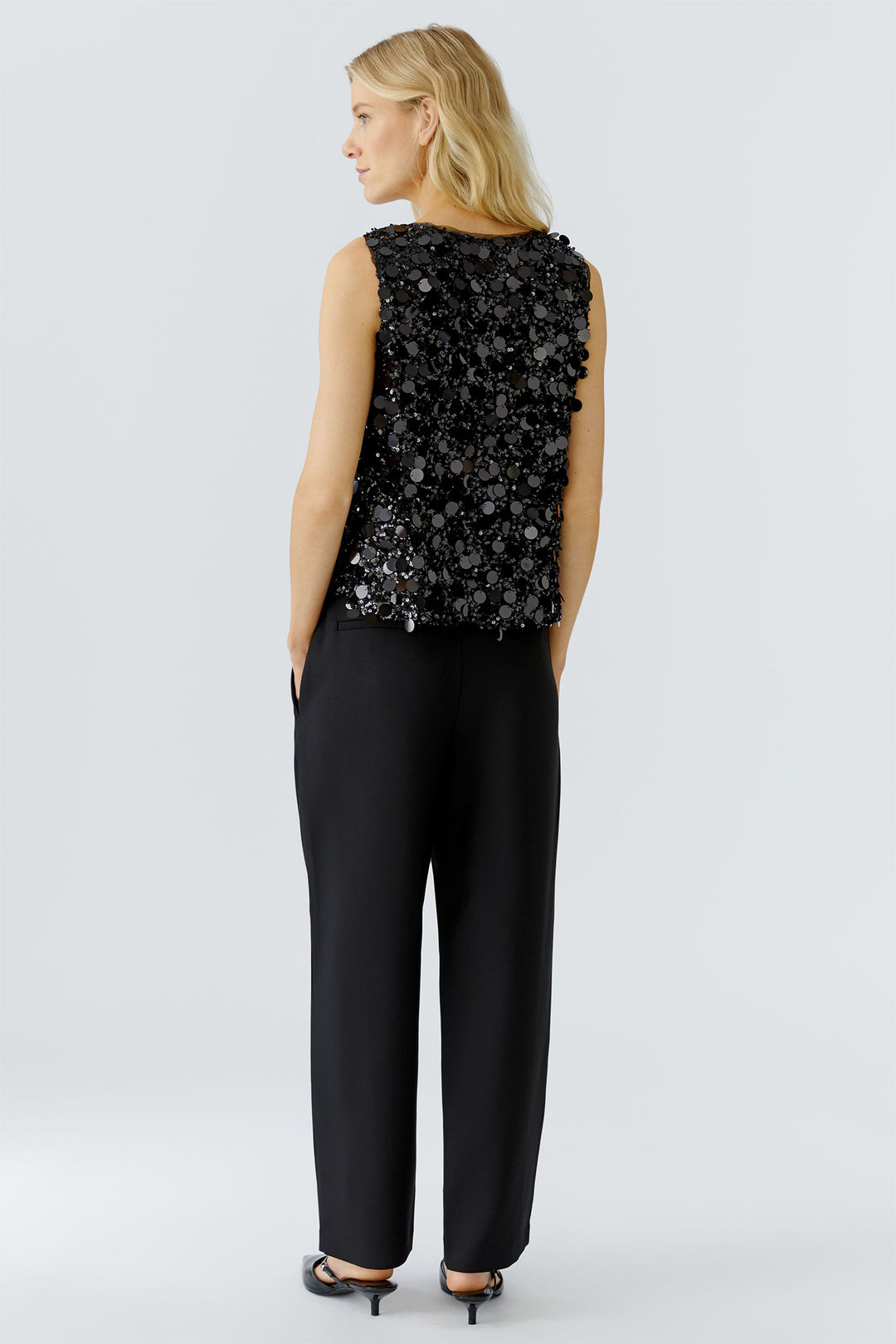 Woman wearing a black sequin top and black pants on a light gray background