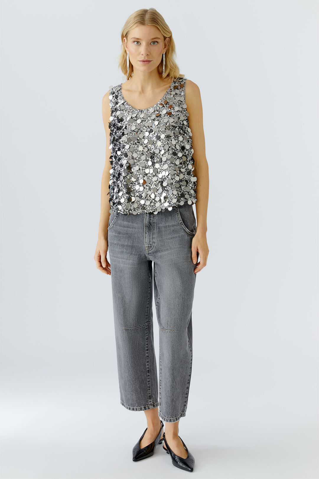 Woman wearing a sequin top and gray jeans on a white background