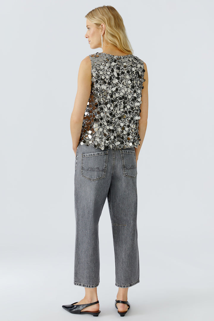 Woman wearing a sleeveless floral top and gray jeans on a white background