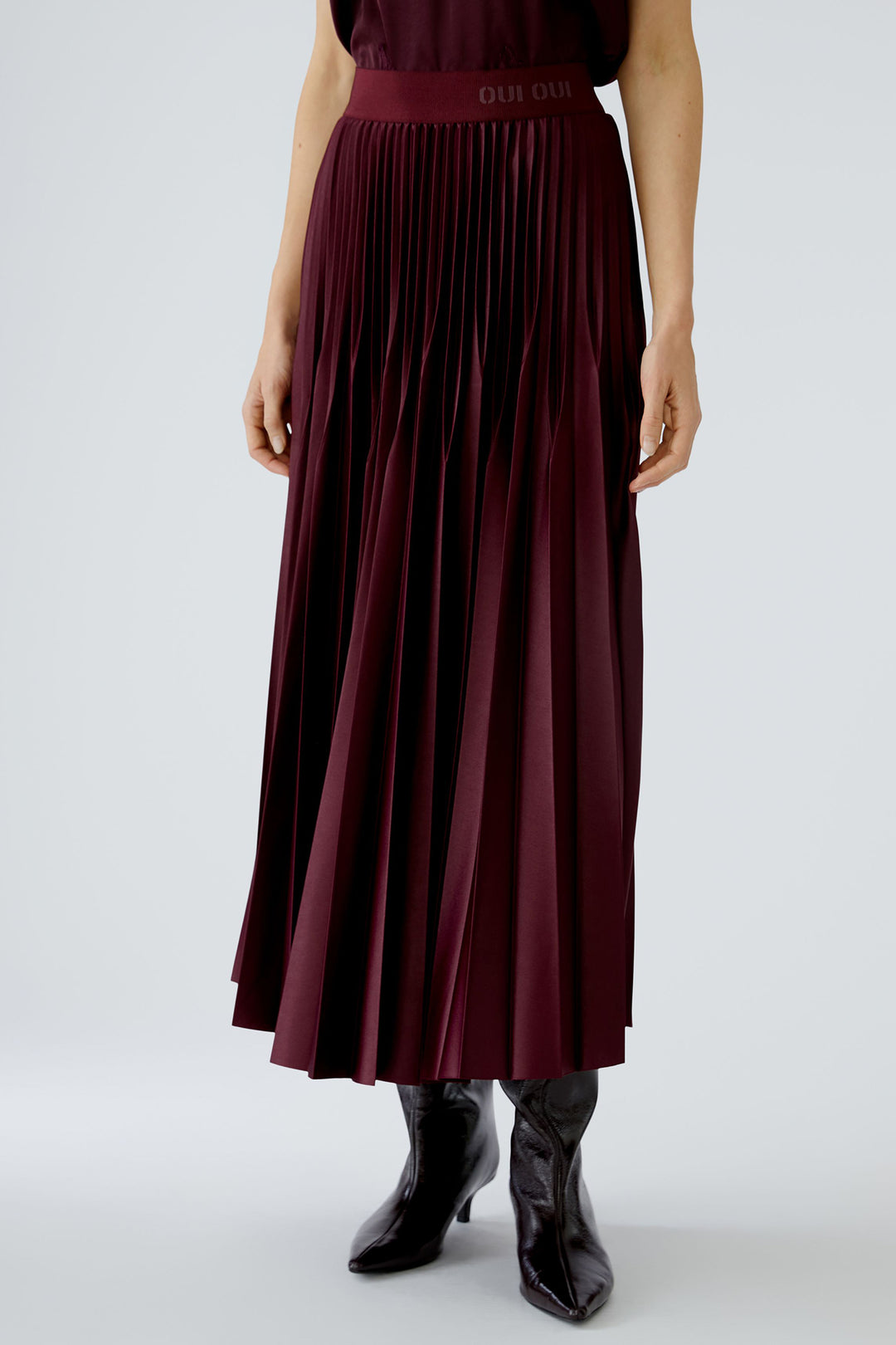 Person wearing a burgundy pleated skirt and black shoes on a white background