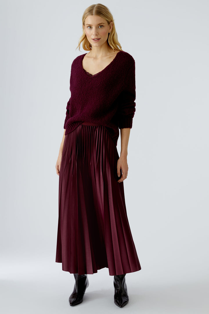 Woman wearing a burgundy sweater and pleated skirt on a white background