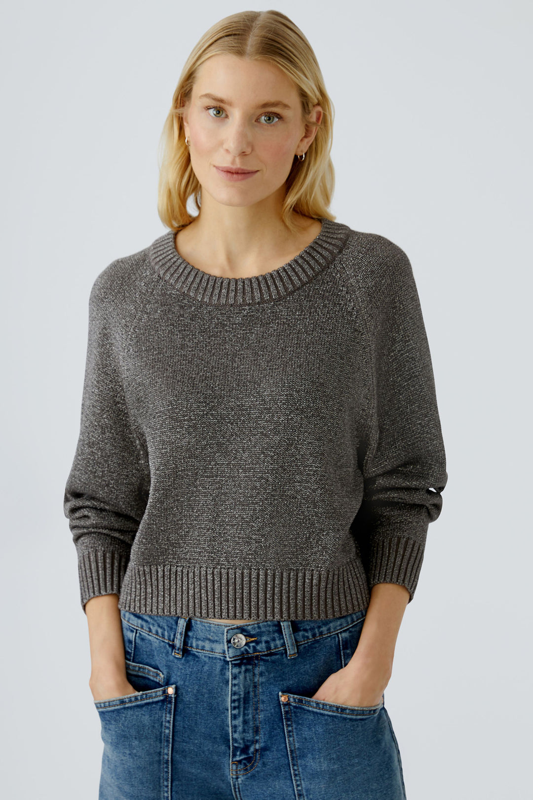 Woman wearing a taupe sweater and blue jeans against a light grey background