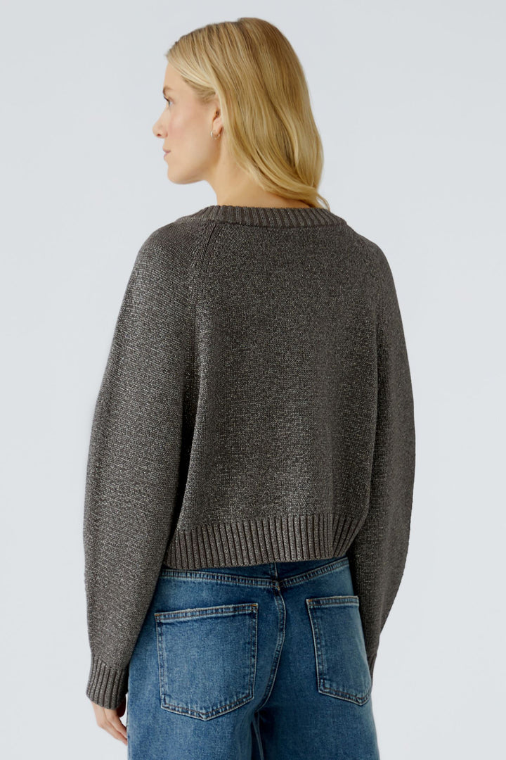 Person wearing a taupe sweater and blue jeans on a light grey background