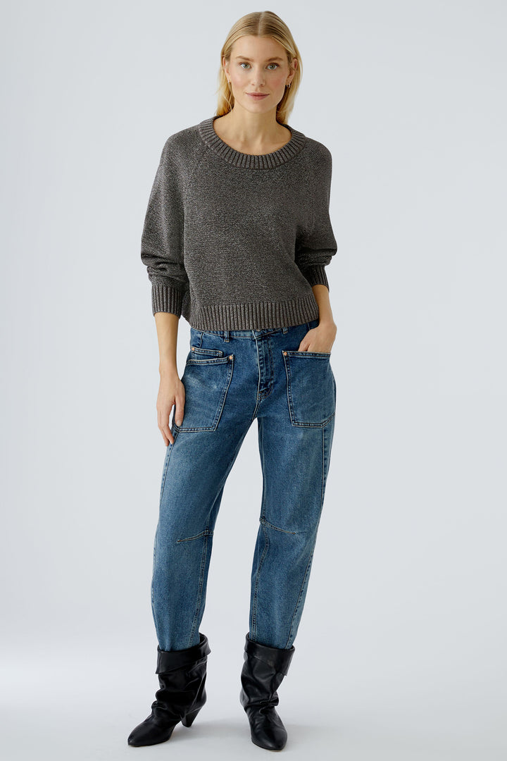 Woman wearing a taupe sweater and blue jeans on a white background