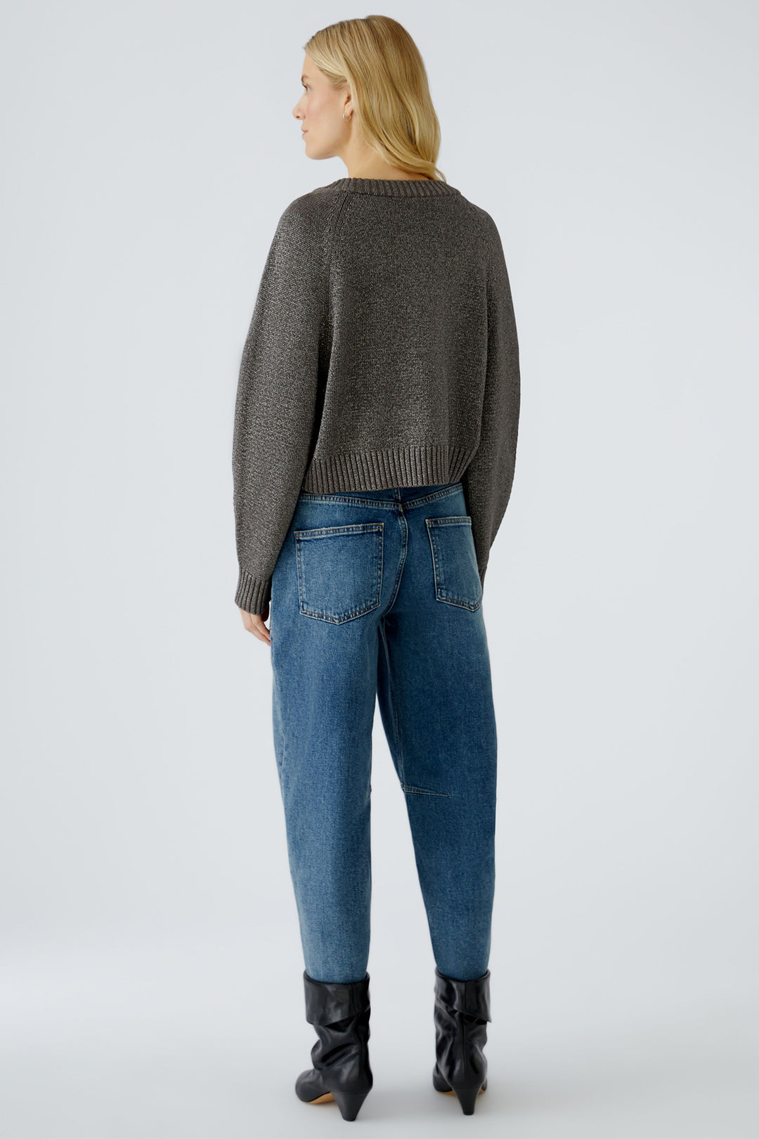 Person wearing a taupe sweater, blue jeans, and black boots on a white background
