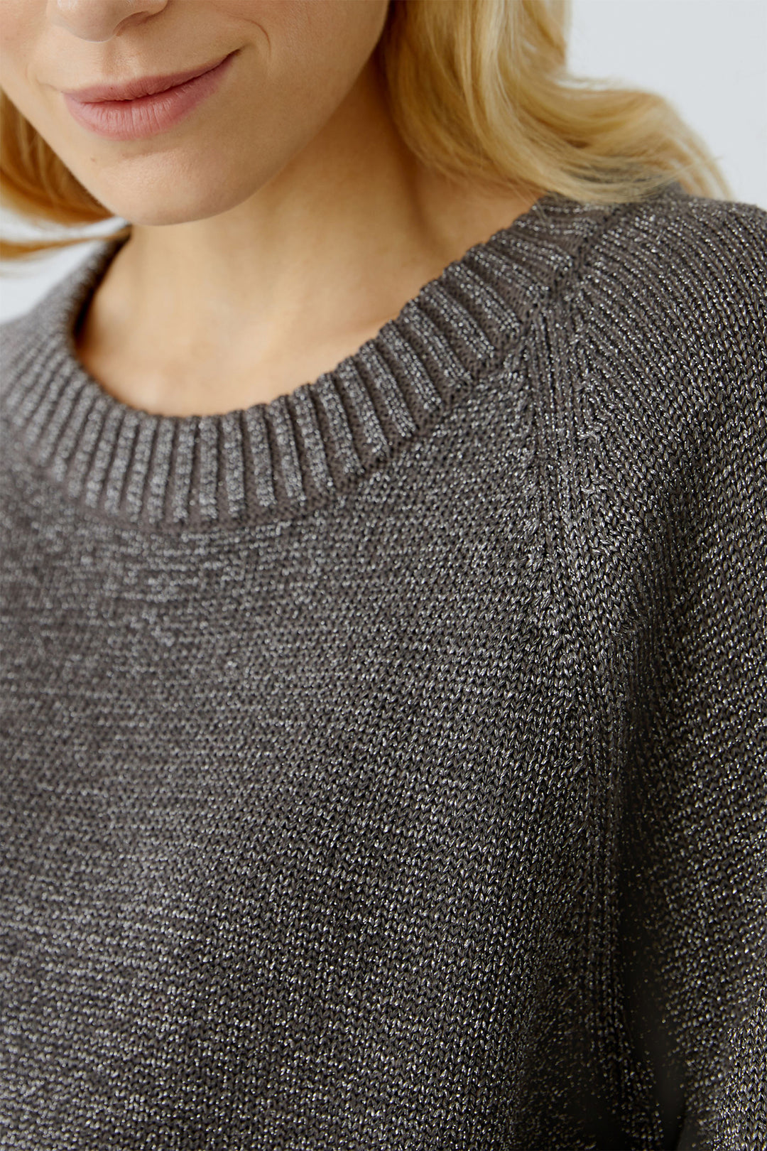 Close-up of a person wearing a taupe knit sweater with a blurred background