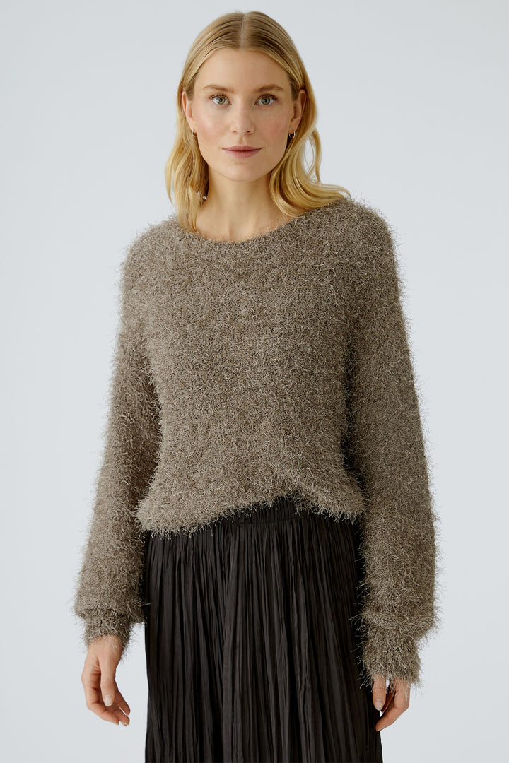 Woman wearing a brown fuzzy sweater and black pleated skirt on a light gray background