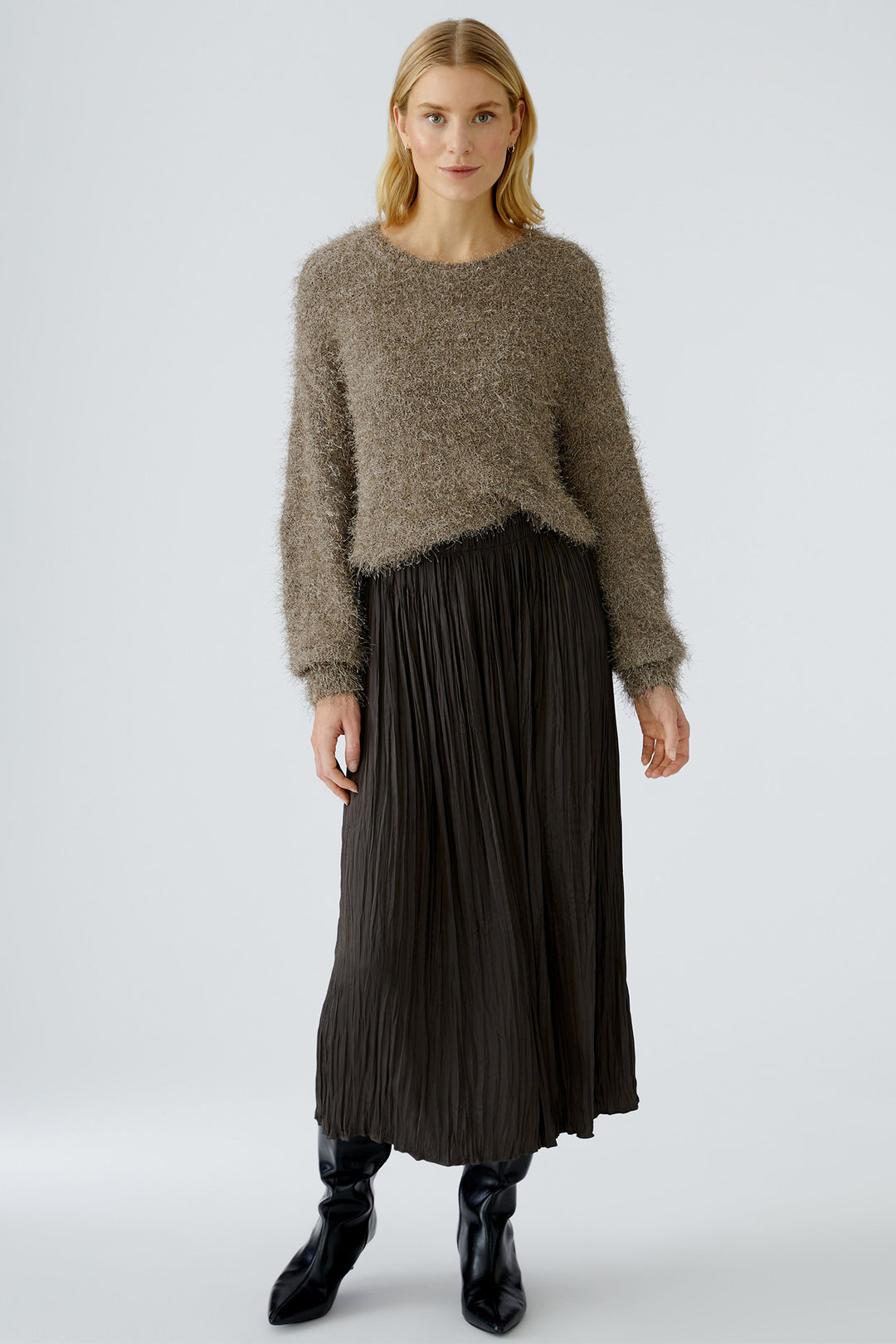 Woman wearing a brown sweater and black pleated skirt on a white background