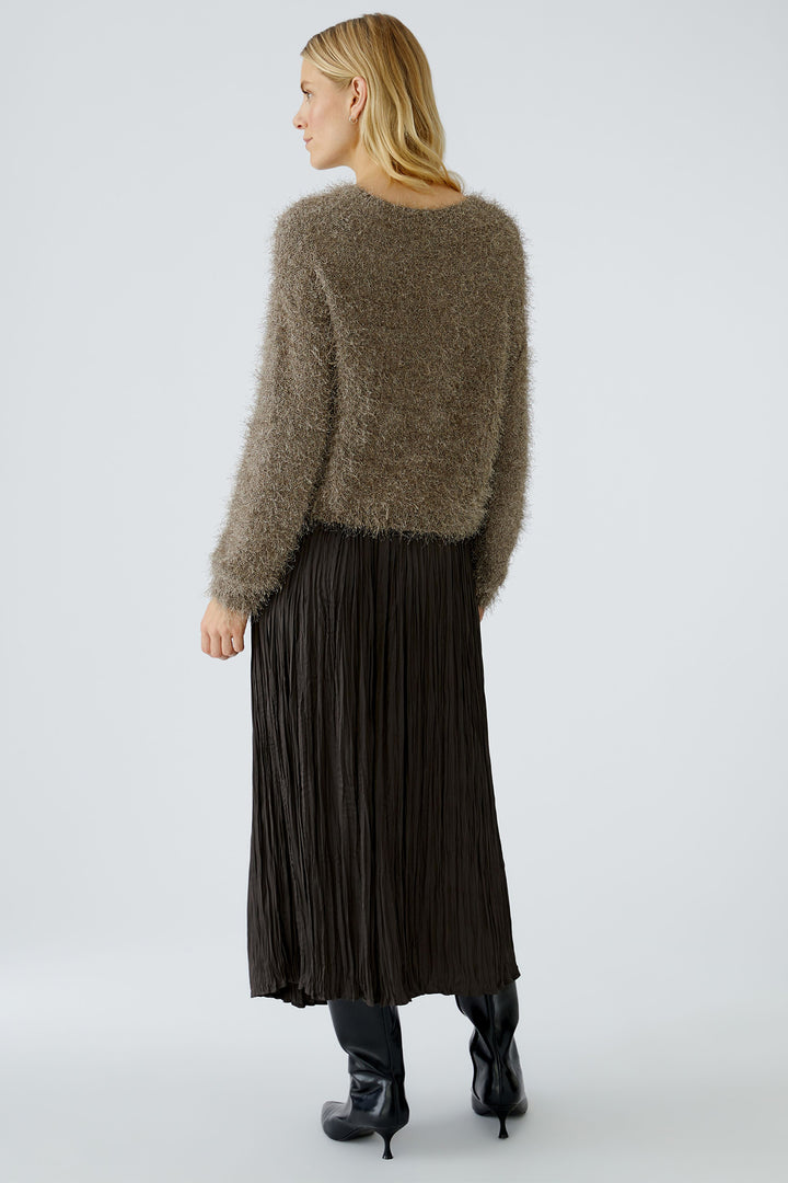 Woman wearing a fluffy brown sweater and black pleated skirt on a white background