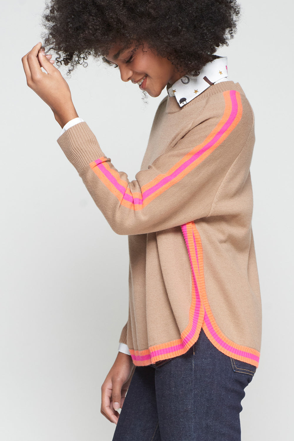 Person wearing a beige cardigan with pink and orange trim on a plain background