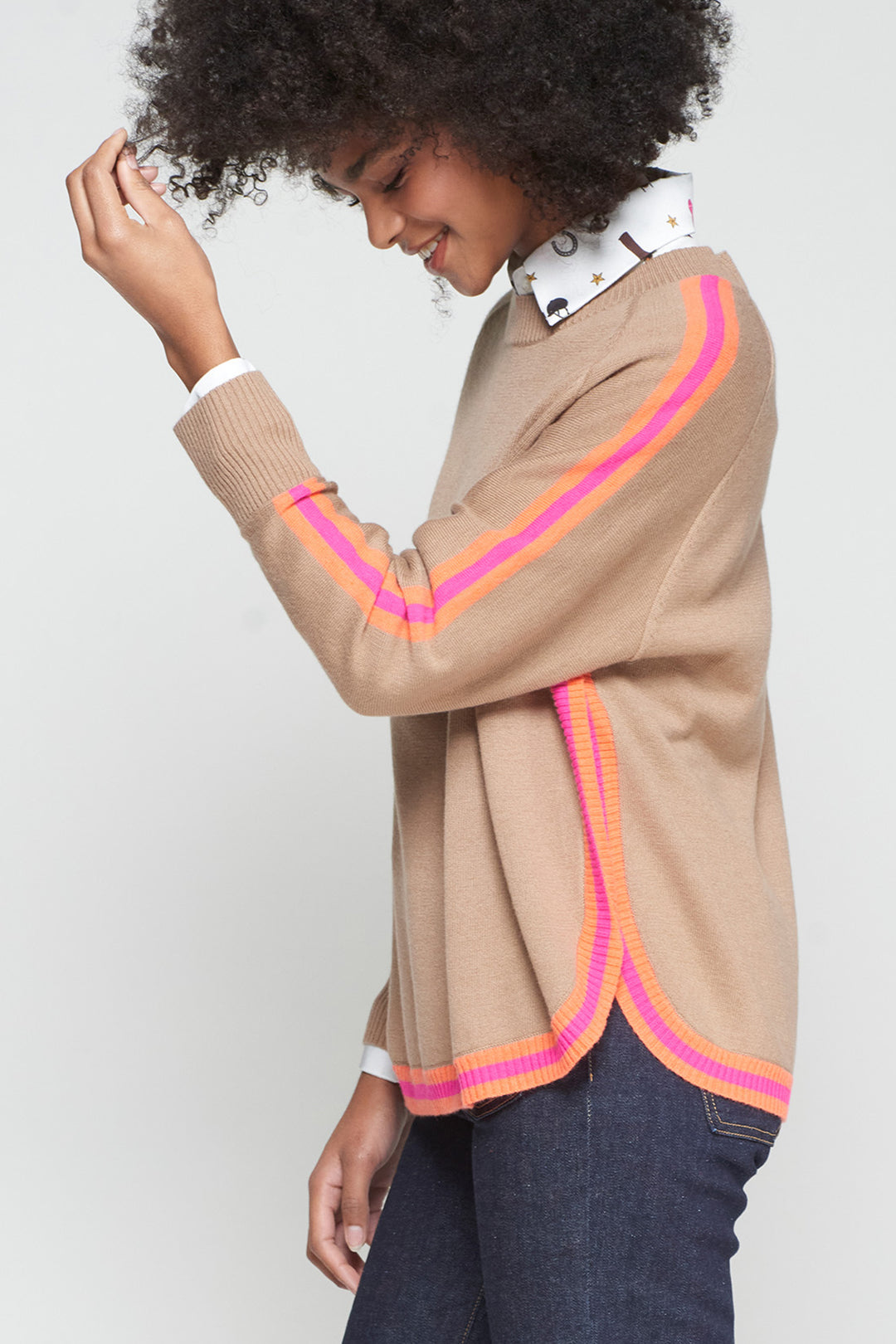 Person wearing a beige cardigan with pink and orange trim on a plain background
