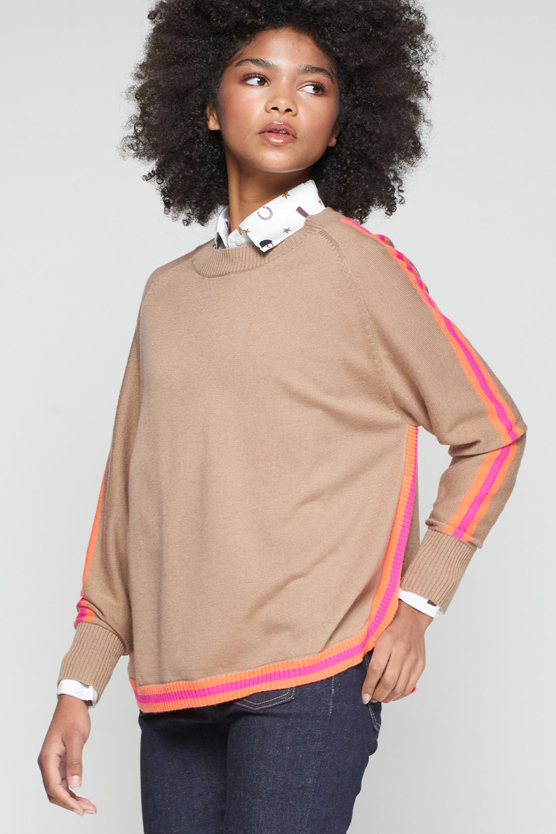 Woman wearing a beige sweater with colorful stripes on a plain background
